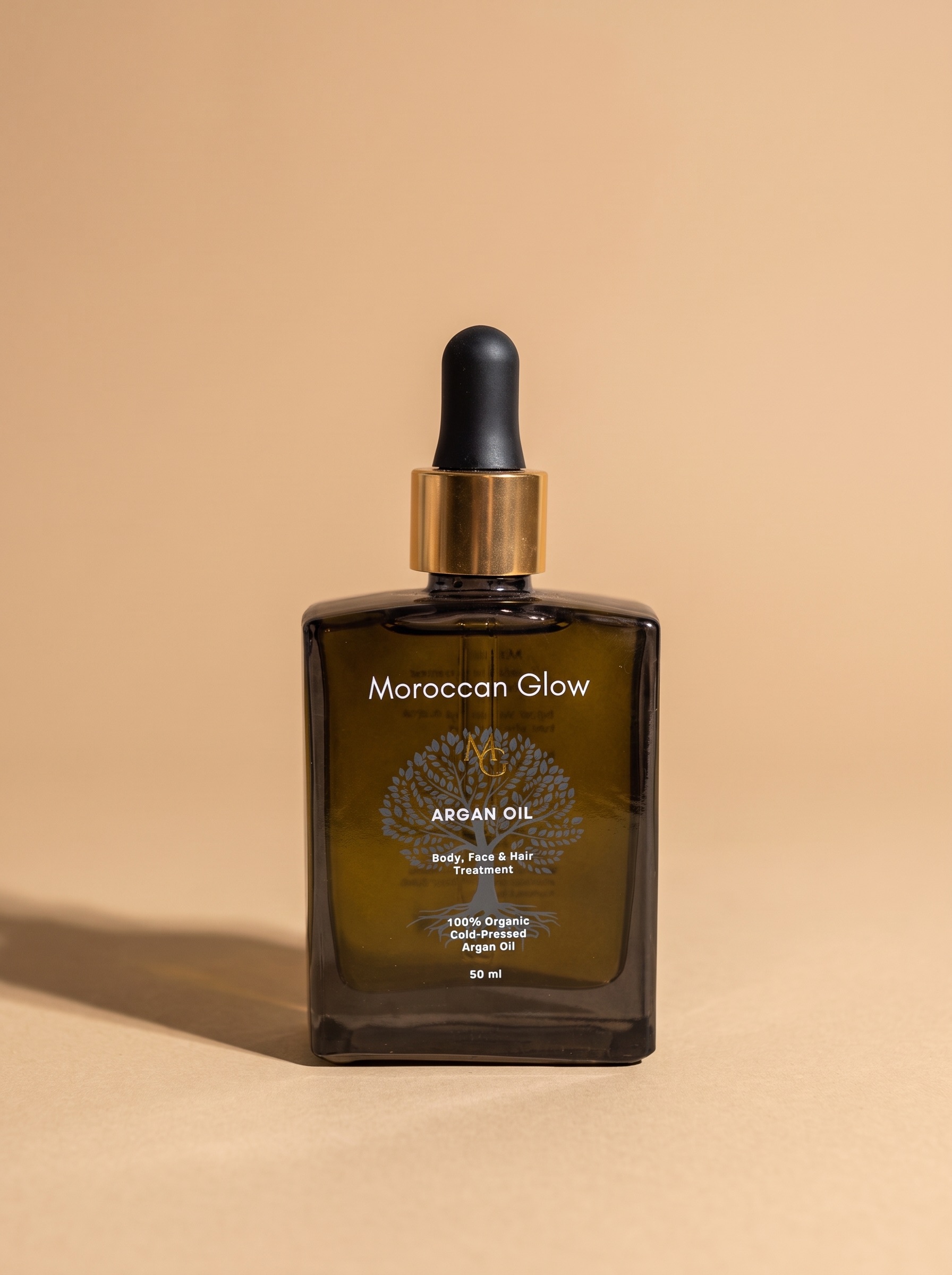 Braunglasflasche Moroccan Glow Arganöl 50 ml mit goldenem Ring und schwarzer Pipette vor beigem Hintergrund